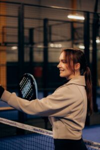 Smiling woman playing paddle tennis indoors with a racket in hand, perfecting her swing.